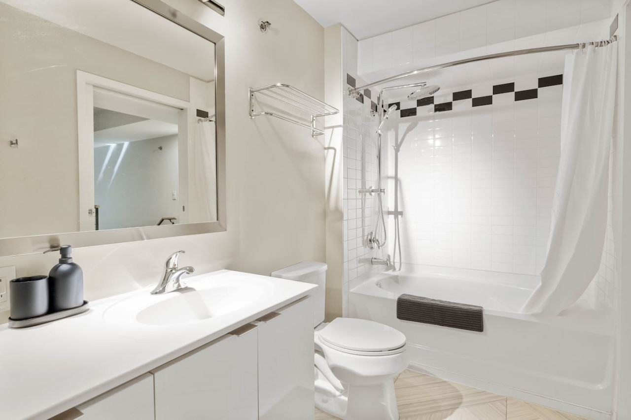 This bright and welcoming bathroom invites you to freshen up in comfort. Enjoy the forest-inspired shower curtain that adds a calming touch to your routine, complemented by the cozy rug underfoot and sparkling clean fixtures.