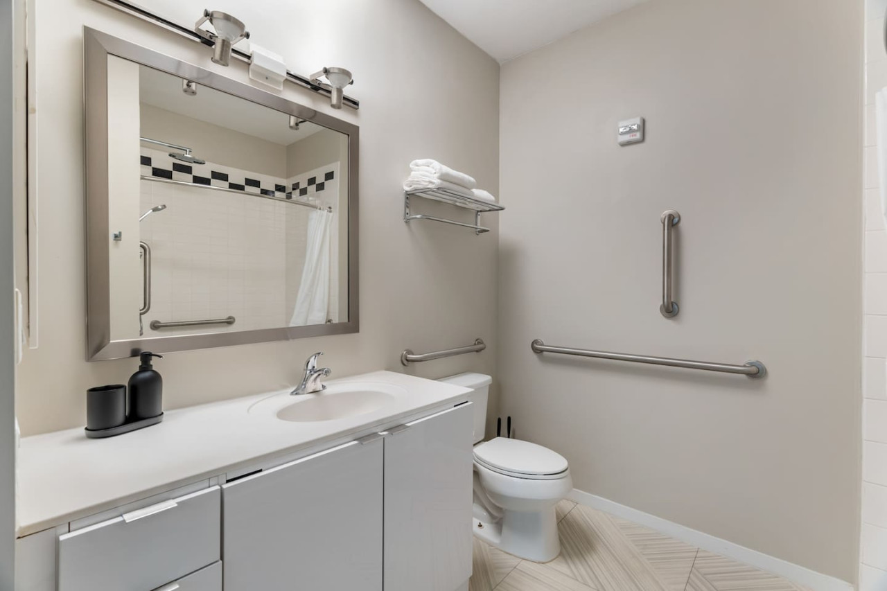 This bright and welcoming bathroom invites you to freshen up in comfort. Enjoy the forest-inspired shower curtain that adds a calming touch to your routine, complemented by the cozy rug underfoot and sparkling clean fixtures.