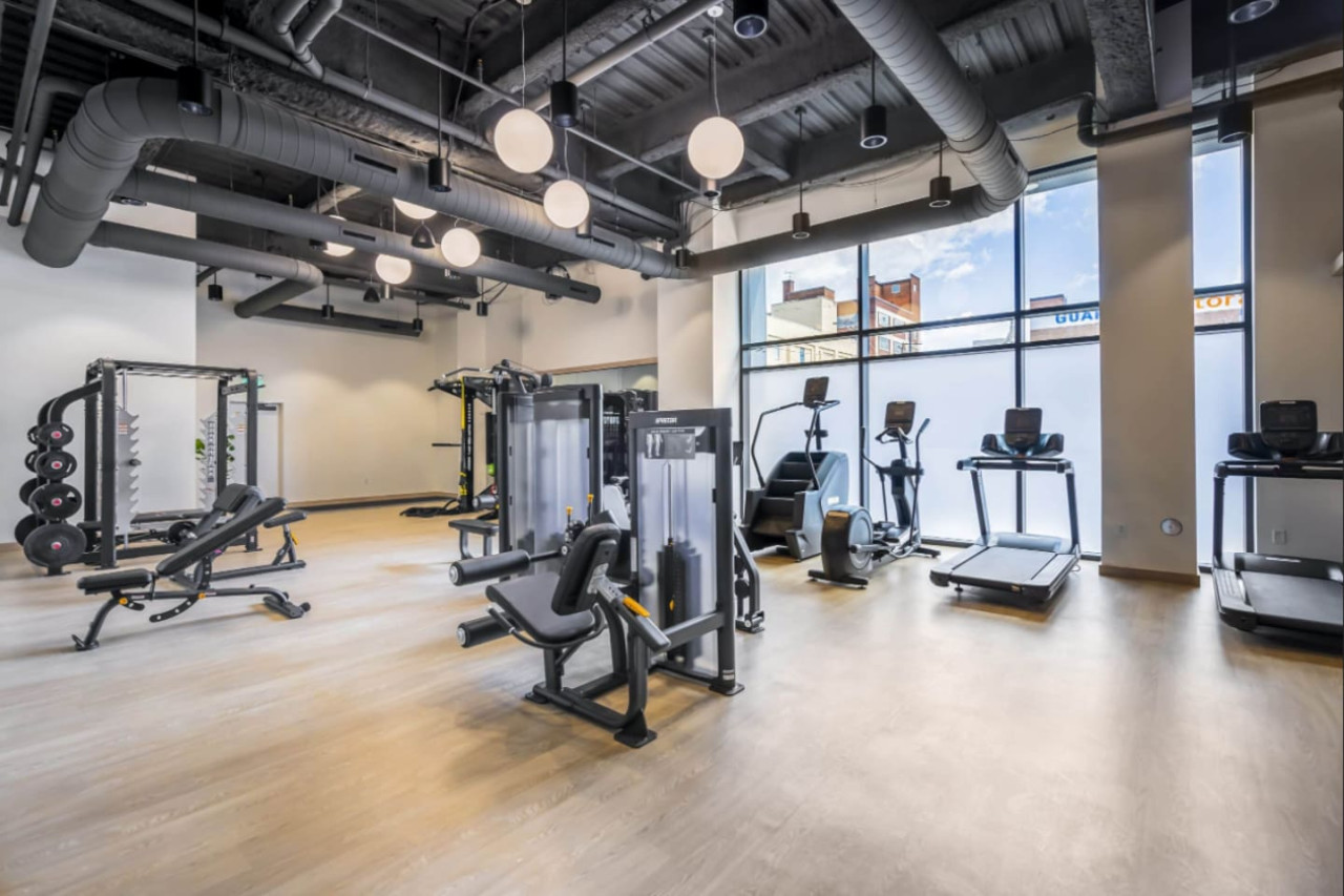Spacious, well-lit gym equipped with a variety of cardio machines, free weights, and strength-training equipment.