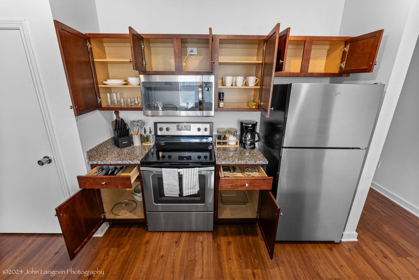 This modern kitchen features a spacious island with cabinetry, sleek white countertops, stainless steel appliances, open shelving, and stylish lighting.