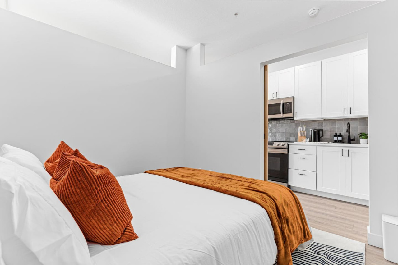 Comfortable Queen size bed - Area rug - Extra pillows w/ Throw blanket - Sliding bedroom door - View of the kitchen through the open bedroom door