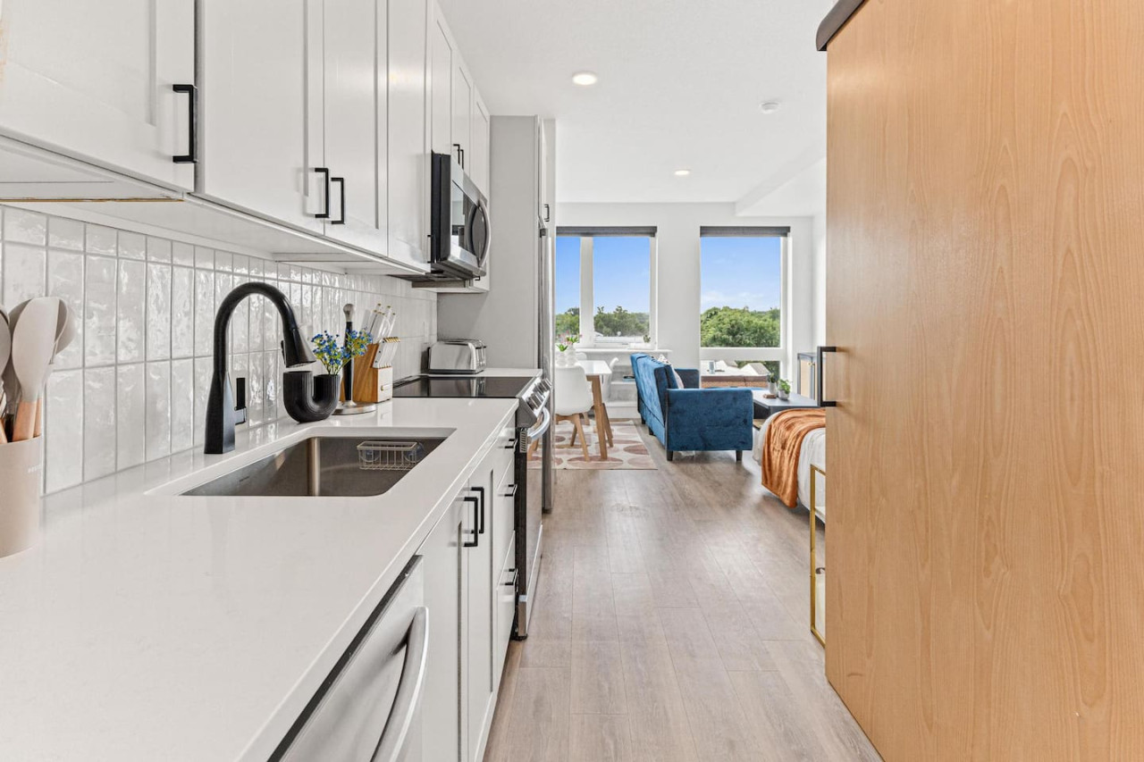 This modern kitchen features a spacious island with cabinetry, sleek white countertops, stainless steel appliances, open shelving, and stylish lighting.