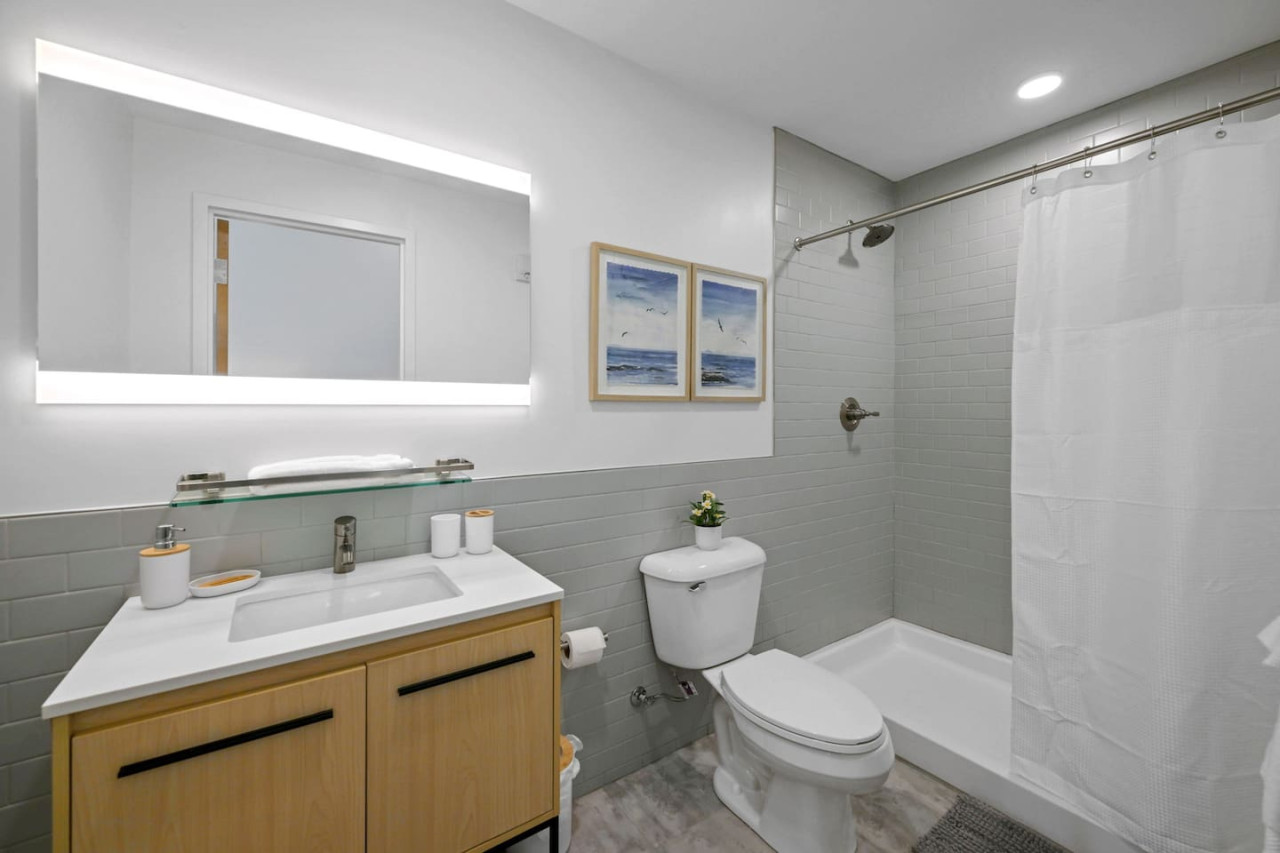 This bright and welcoming bathroom invites you to freshen up in comfort. Enjoy the forest-inspired shower curtain that adds a calming touch to your routine, complemented by the cozy rug underfoot and sparkling clean fixtures.