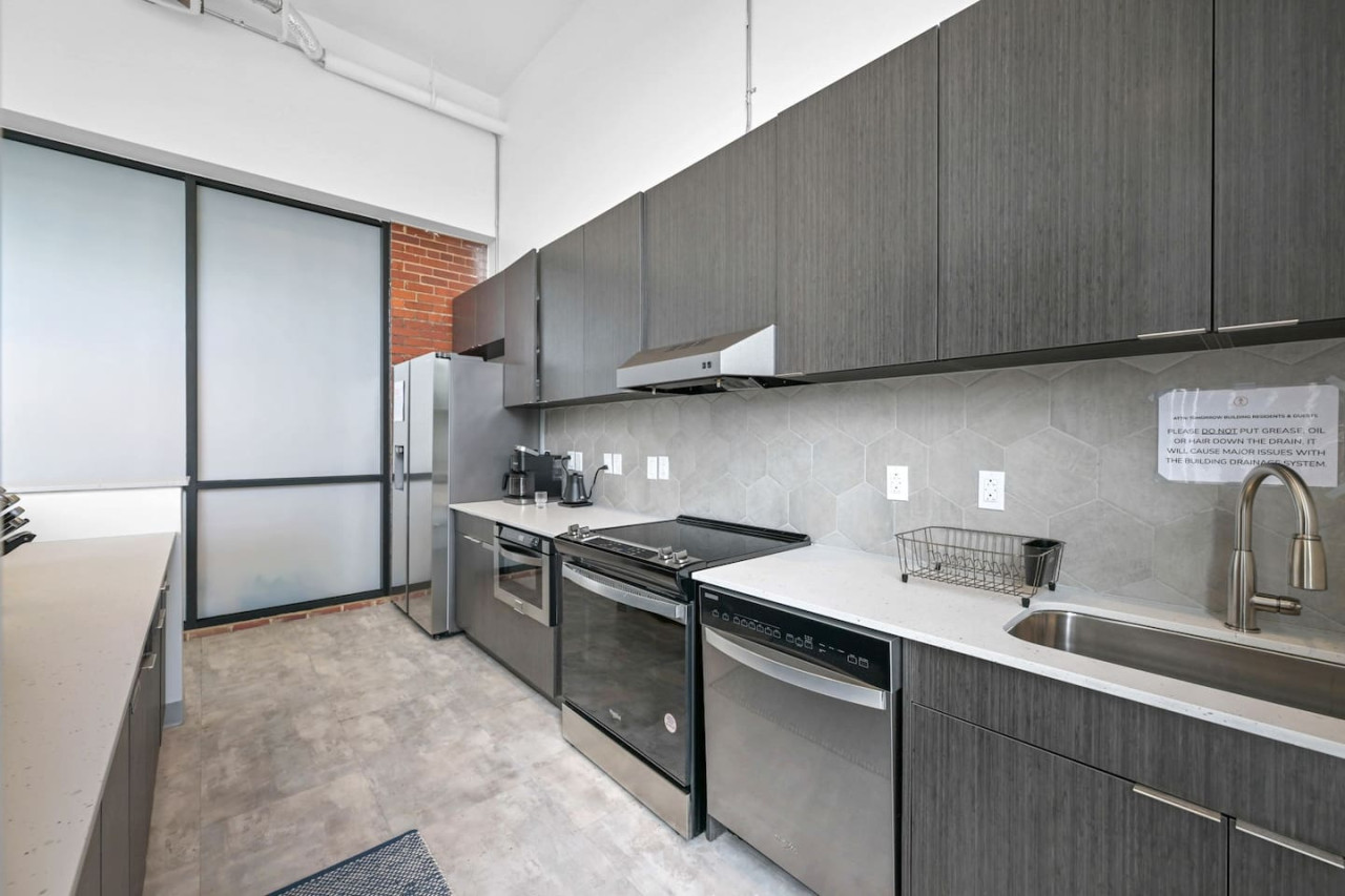 This modern kitchen features a spacious island with cabinetry, sleek white countertops, stainless steel appliances, open shelving, and stylish lighting.