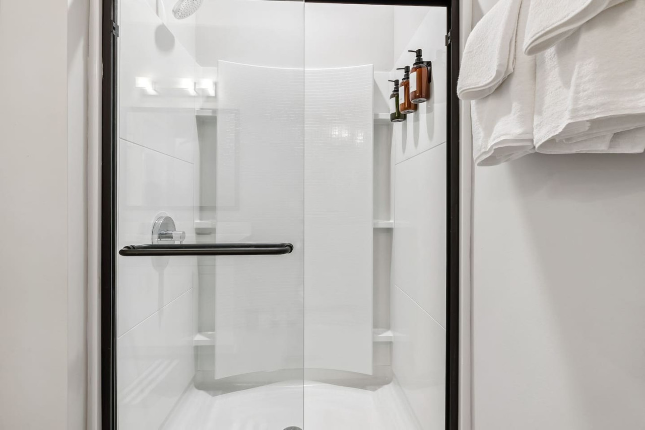 This bright and welcoming bathroom invites you to freshen up in comfort. Enjoy the forest-inspired shower curtain that adds a calming touch to your routine, complemented by the cozy rug underfoot and sparkling clean fixtures.