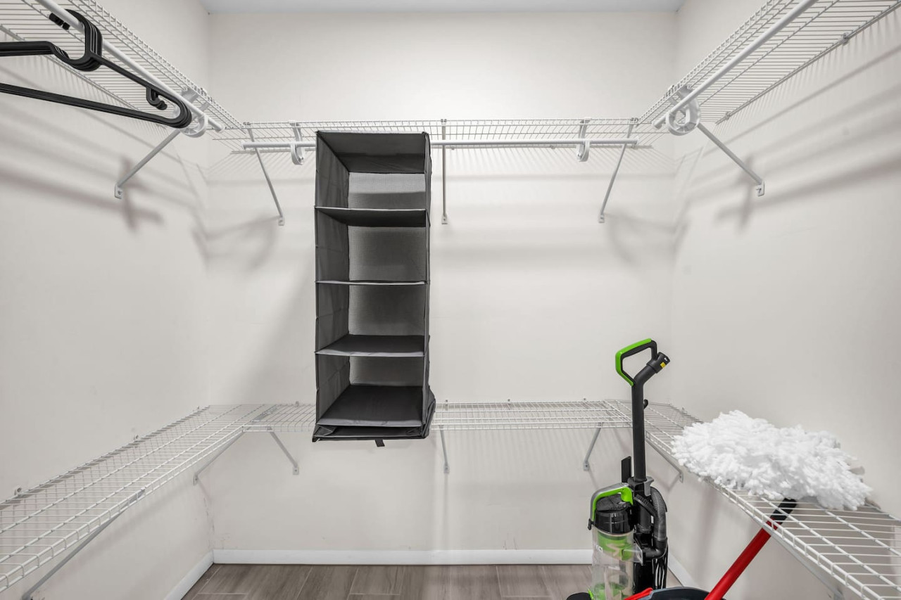 Spacious walk-in closet equipped with shelving, ample storage space, and cleaning essentials for guest use.