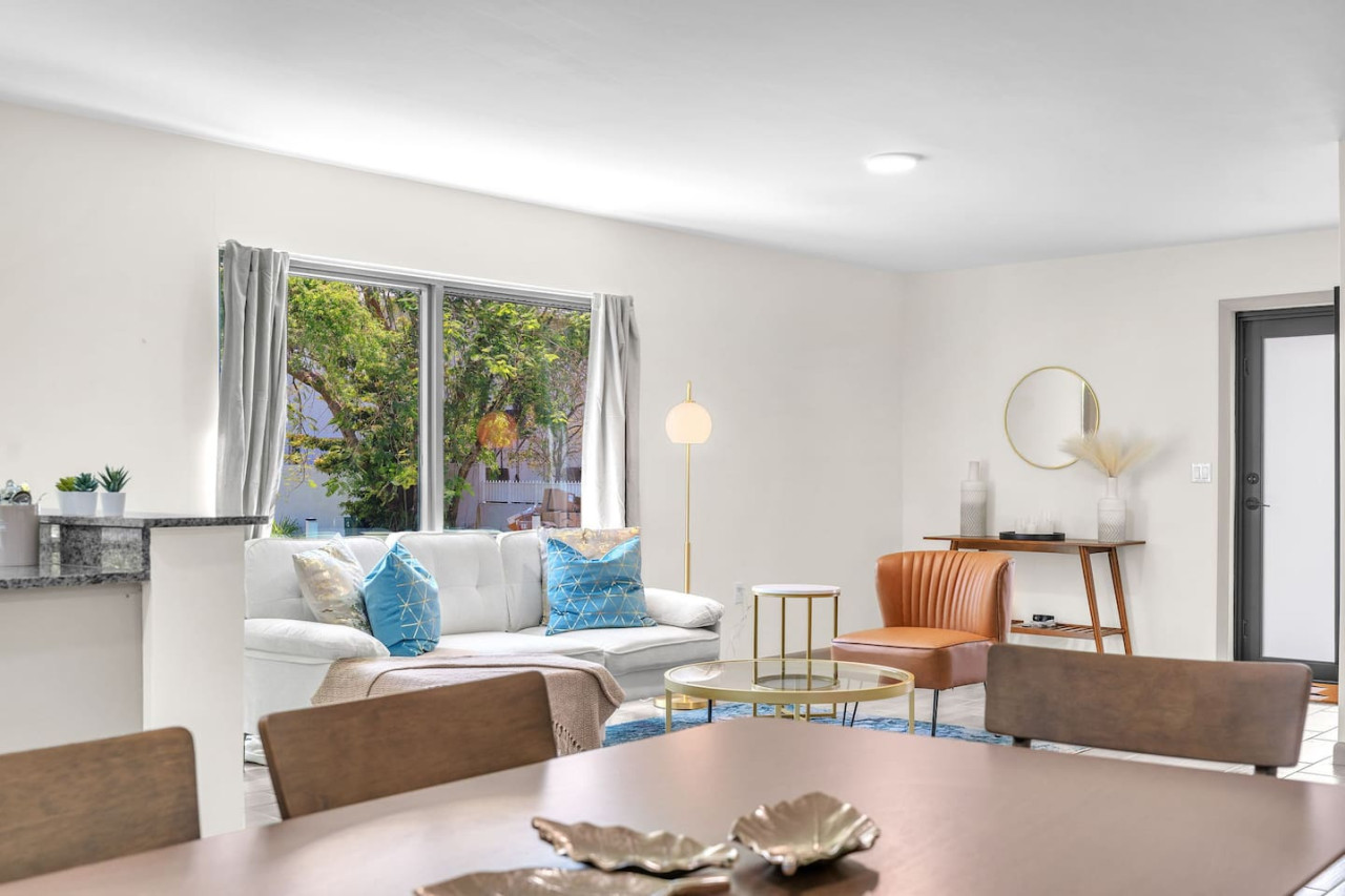 Elegant living area featuring a white sofa with bright blue and metallic accent pillows, paired with a glass coffee table.