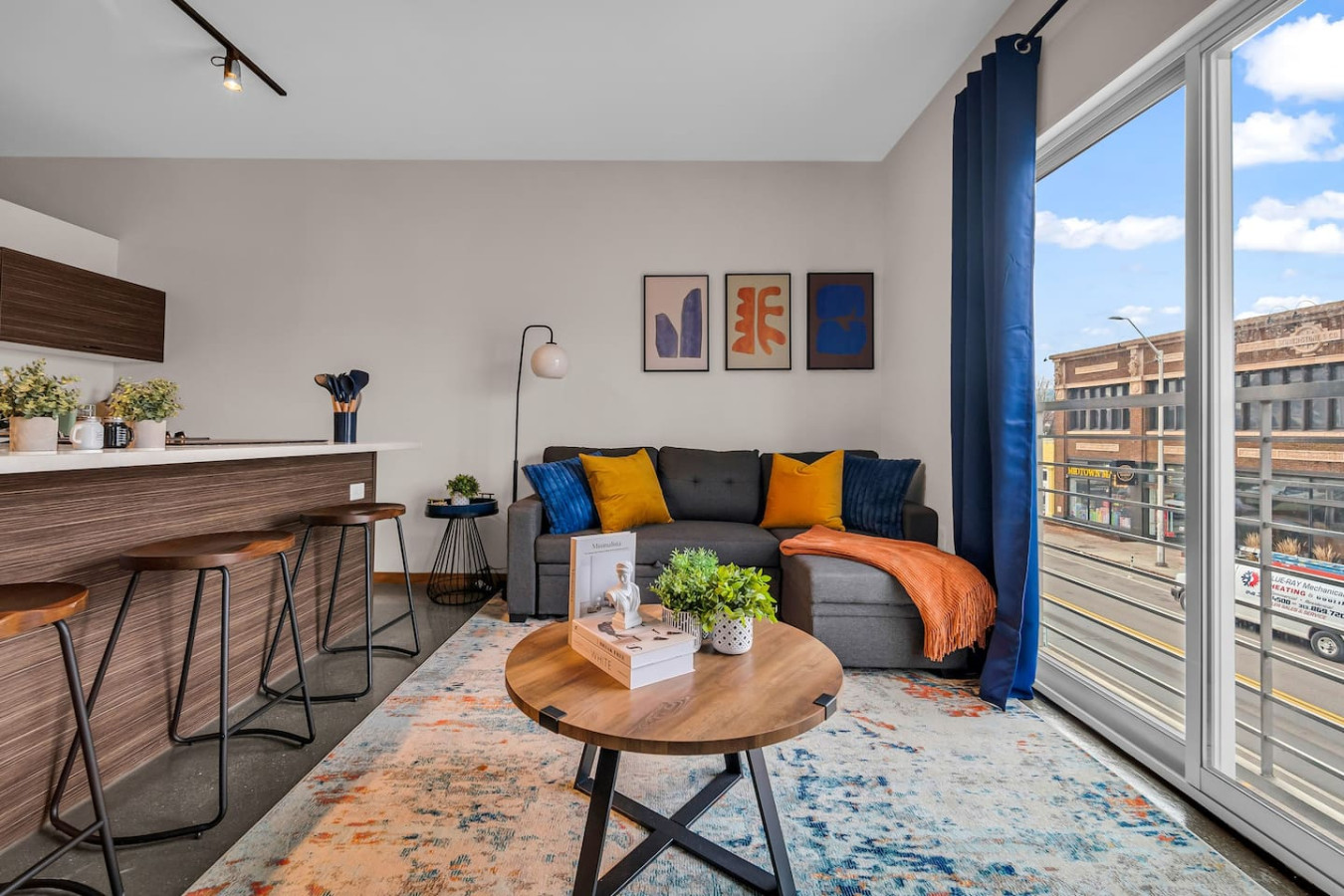 Spacious open-concept living and dining area featuring a vibrant blue sofa, modern furnishings, and a stylish entertainment setup—ideal for gatherings and relaxation.