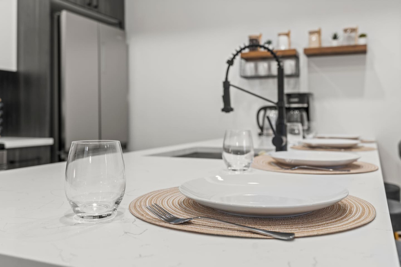 This modern kitchen features a spacious island with bold blue cabinetry, sleek white countertops, stainless steel appliances, open shelving, and stylish lighting.