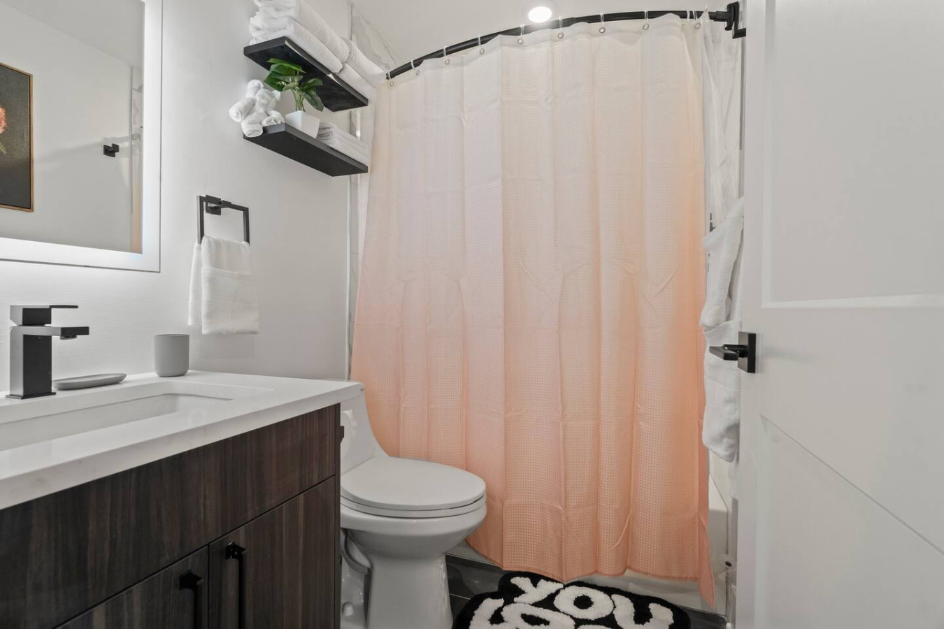 Modern bathroom with bath mat, toilet, shower area, and linens.