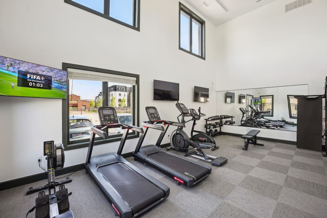 Spacious, well-lit gym equipped with a variety of cardio machines, free weights, and strength-training equipment.