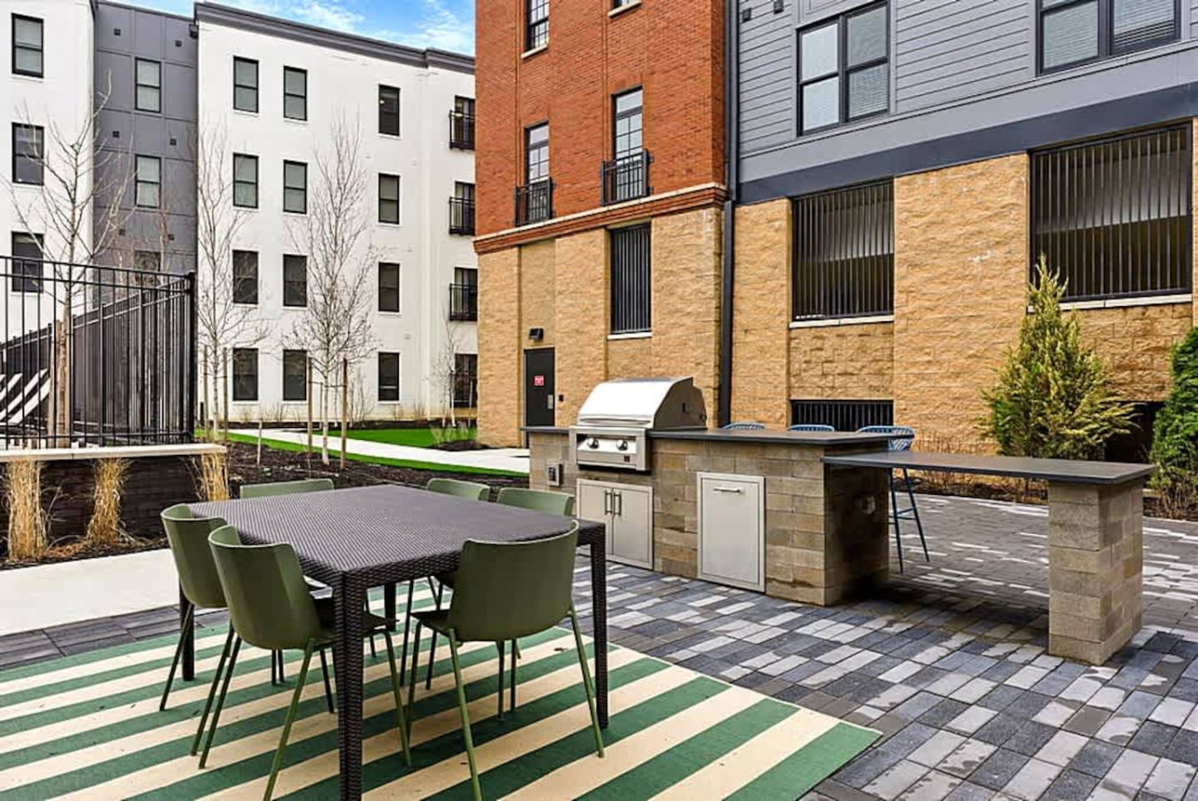 An outdoor dining area beside a high quality grill station, offering comfortable seating and a stylish layout. Guests can enjoy cooking outdoors or relaxing in a bright courtyard atmosphere designed for social moments.