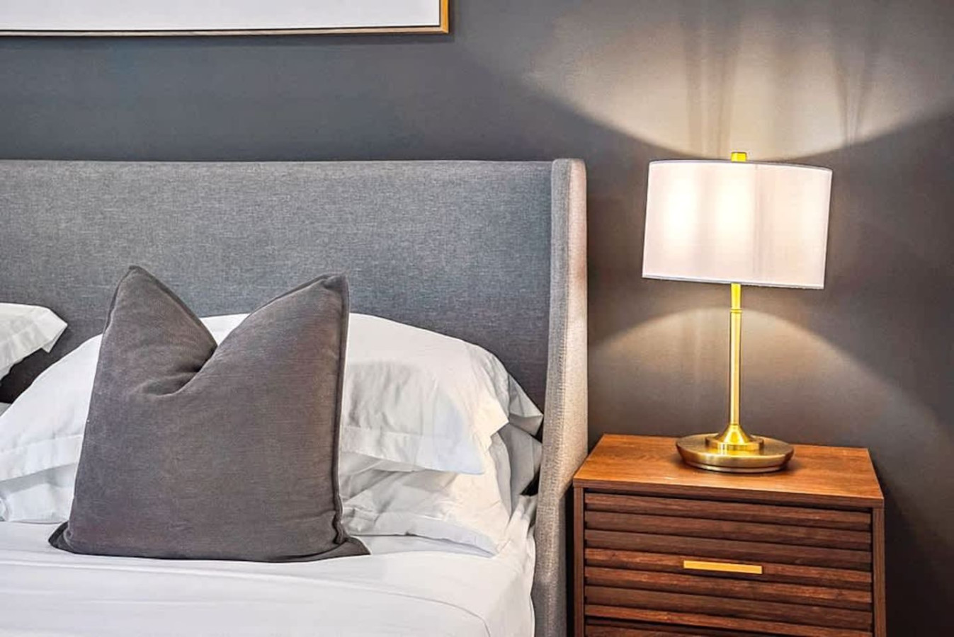 A warm and inviting bedroom with a plush gray headboard, soft bedding, and bedside lighting. This cozy setup creates a peaceful atmosphere perfect for restful nights and relaxing mornings.