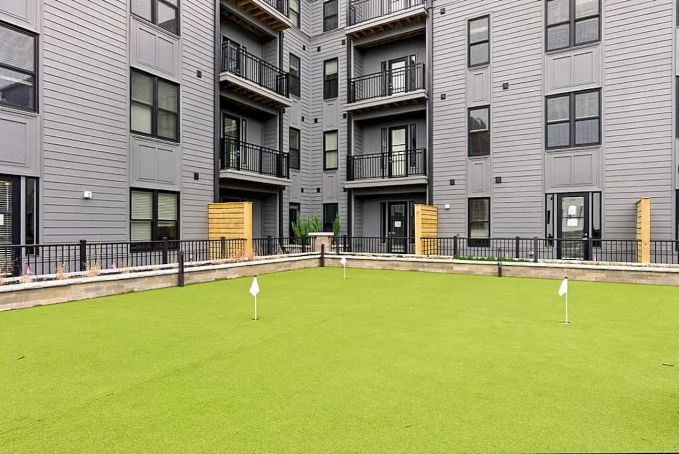 A beautiful green courtyard with manicured turf surrounded by modern apartment facades. This open space is perfect for relaxing outdoors, enjoying fresh air, or spending time in a peaceful community atmosphere.