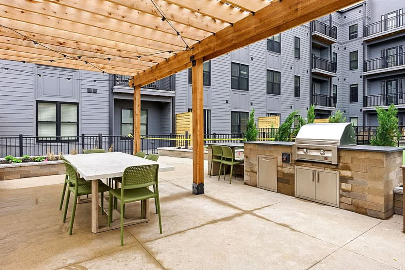 A shaded outdoor seating area featuring a pergola, dining table, and nearby grilling station. Ideal for shared meals, relaxing afternoons, or simply enjoying the outdoor amenities in a comfortable designed space.
