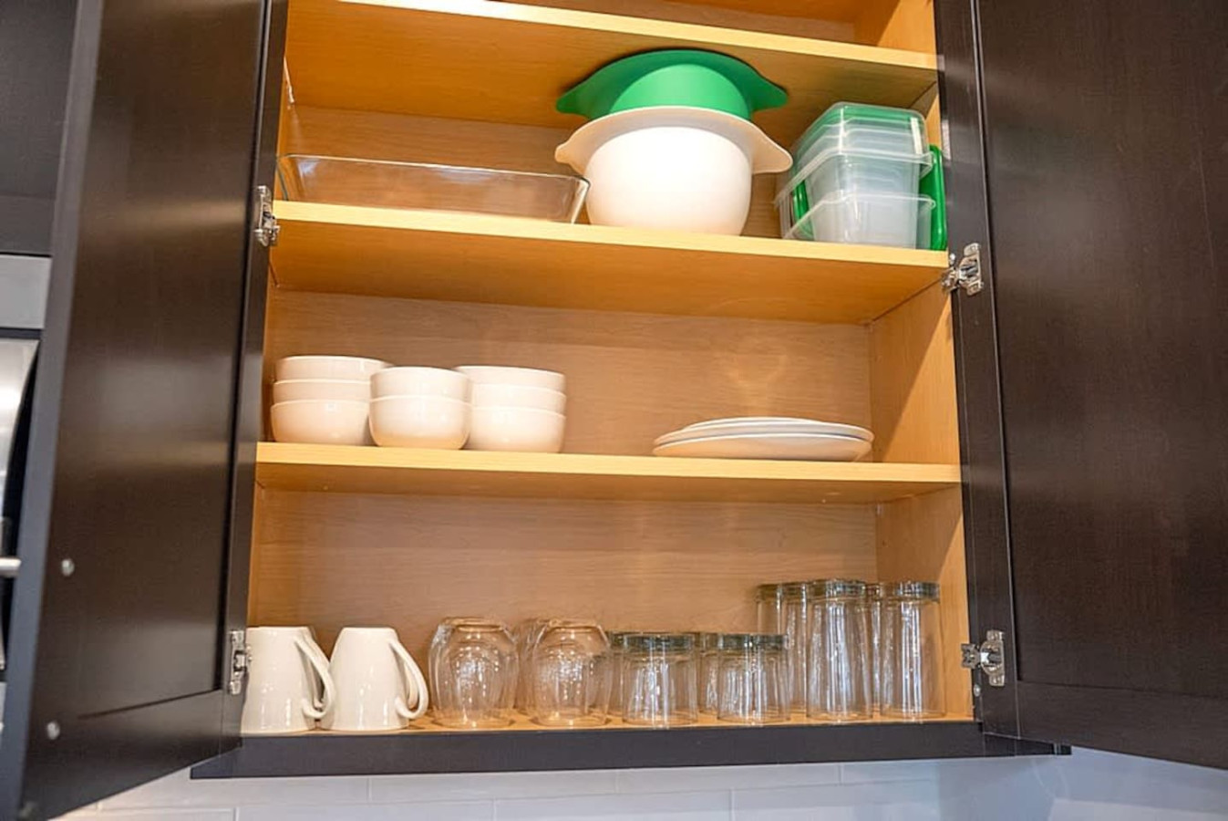 Open cabinets reveal neatly arranged dishes, cups, and glasses. This organized storage helps guests feel at home with everything easily accessible for meals and refreshments.
