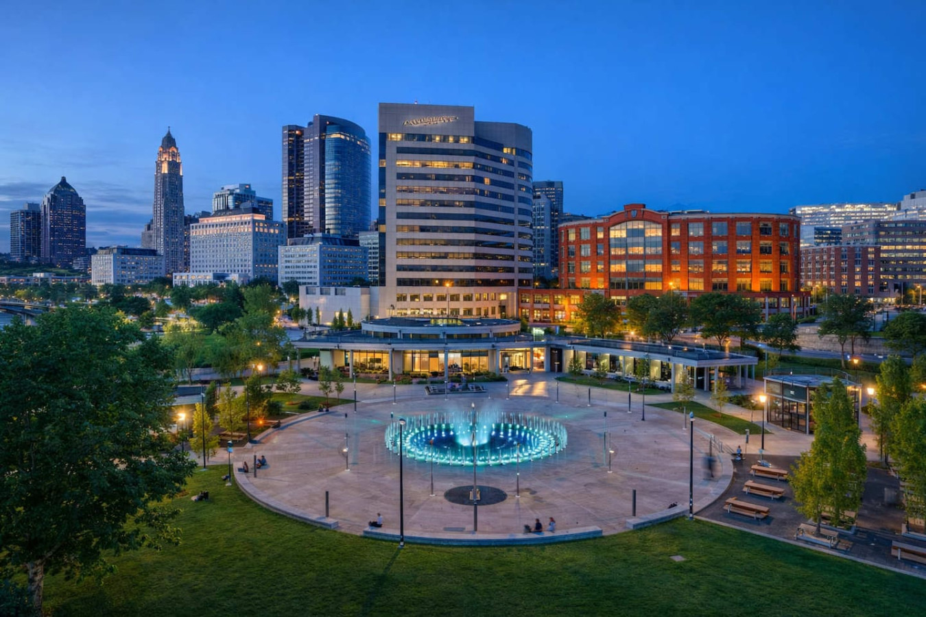 Vibrant downtown riverfront with skyline views, open green spaces, and a central fountain. Perfect for evening strolls, outdoor events, and enjoying the lively energy of the city both day and night.