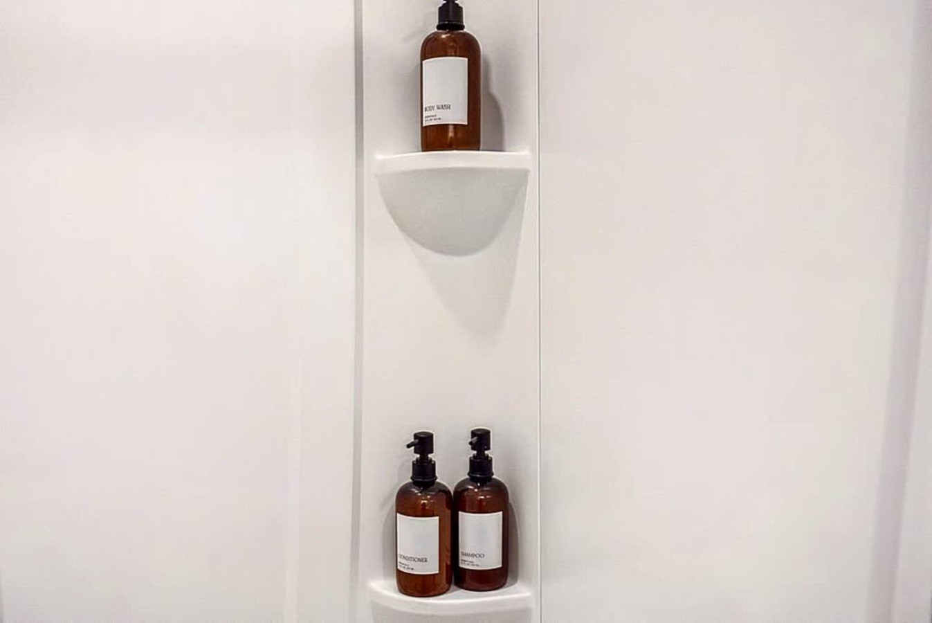 A clean and modern shower area stocked with premium bath products. The minimalist shelving and bright white finishes create a refreshing environment ideal for daily routines.