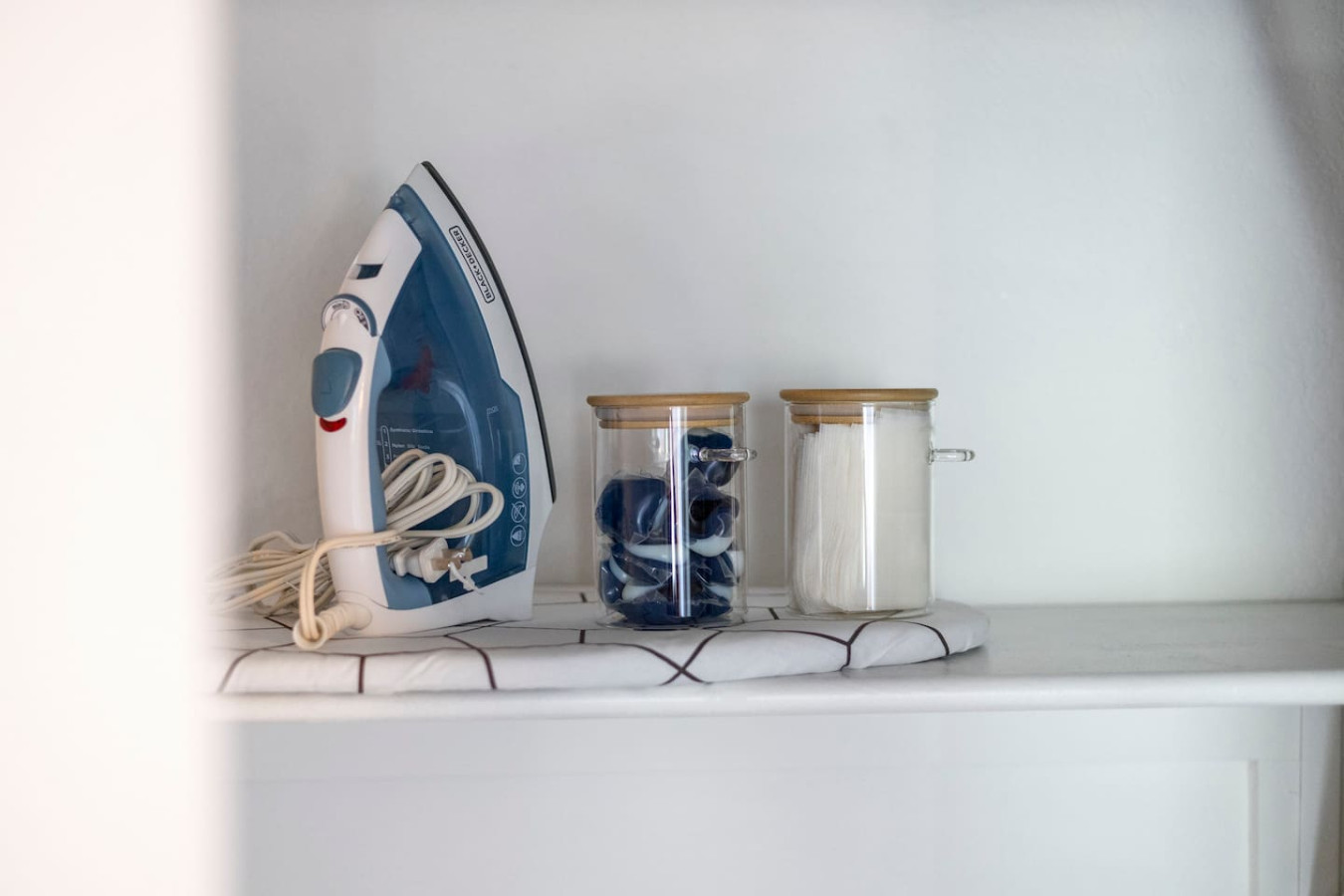 Laundry area is equipped with laundry detergent, pods, iron, and iron board.