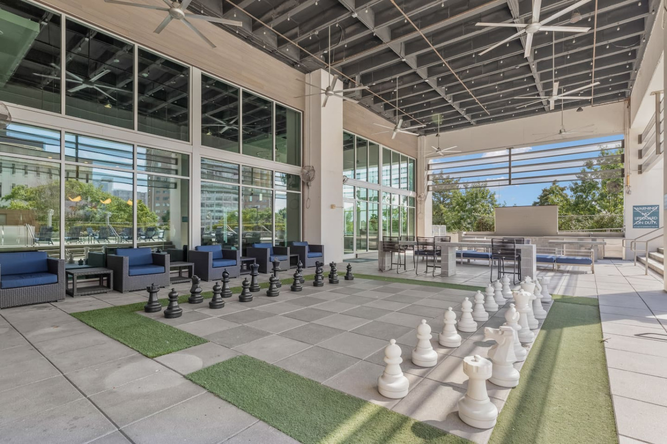 Covered outdoor lounge with life-size chess, comfortable seating, and ceiling fans — steps from the rooftop pool area. A unique amenity space to unwind and enjoy the Atlanta weather with friends.