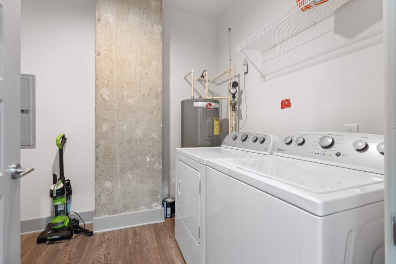 Private laundry room with full-size Whirlpool washer and dryer, wire shelving for storage, and a vacuum for your convenience. A rare perk for a downtown Atlanta high-rise stay.