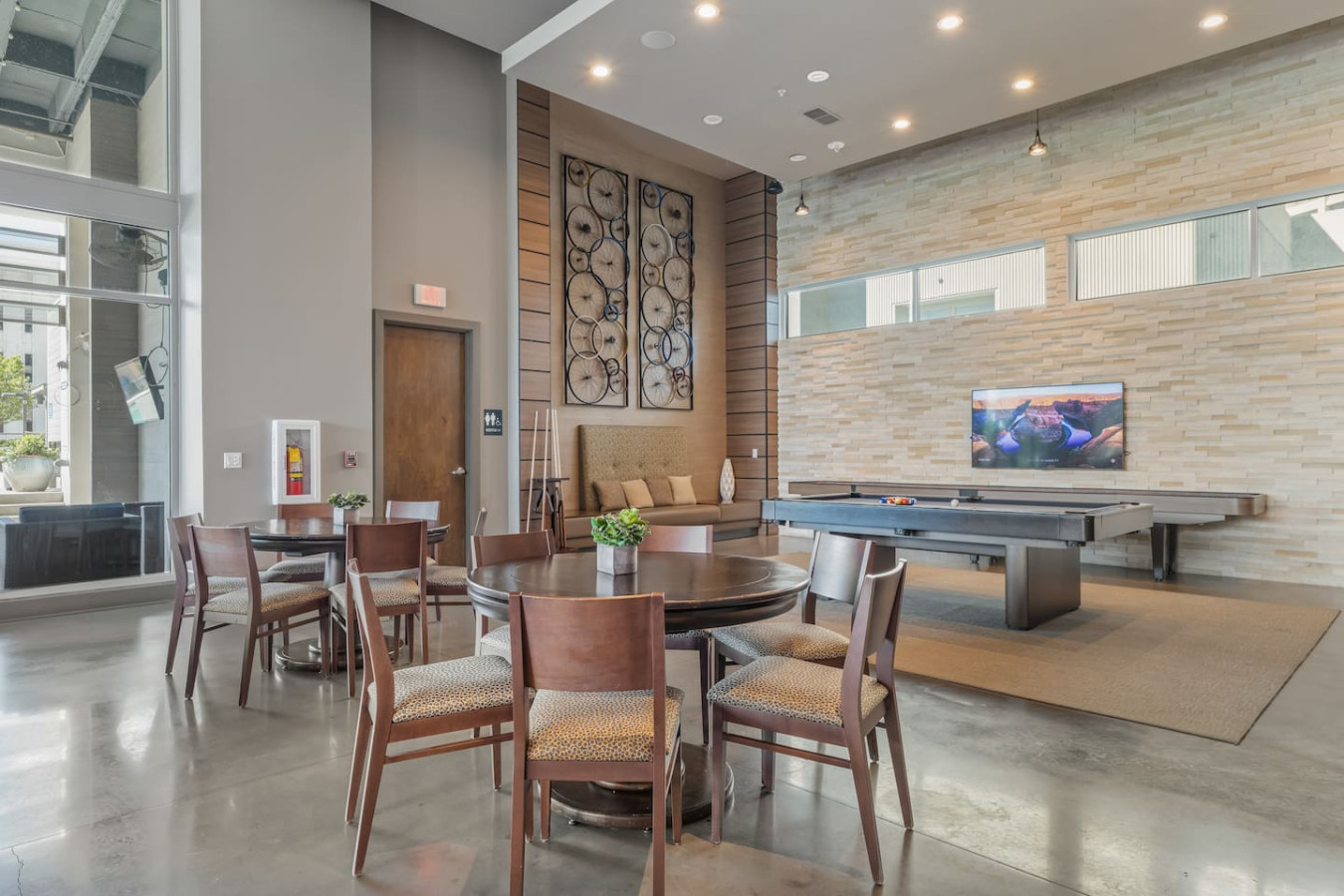 Building game room featuring a pool table and shuffleboard against a stacked stone accent wall. Stylish lounge seating and unique bicycle-wheel art create a fun hangout spot for guests of all ages.