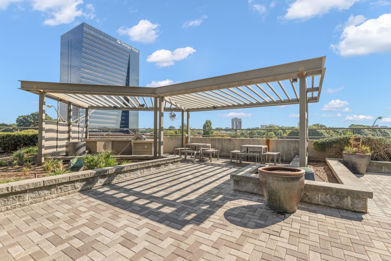 Rooftop terrace with a pergola-covered grilling and dining area, panoramic views of the Atlanta skyline, and lush landscaping. The perfect spot for an evening cookout or relaxing under open skies.