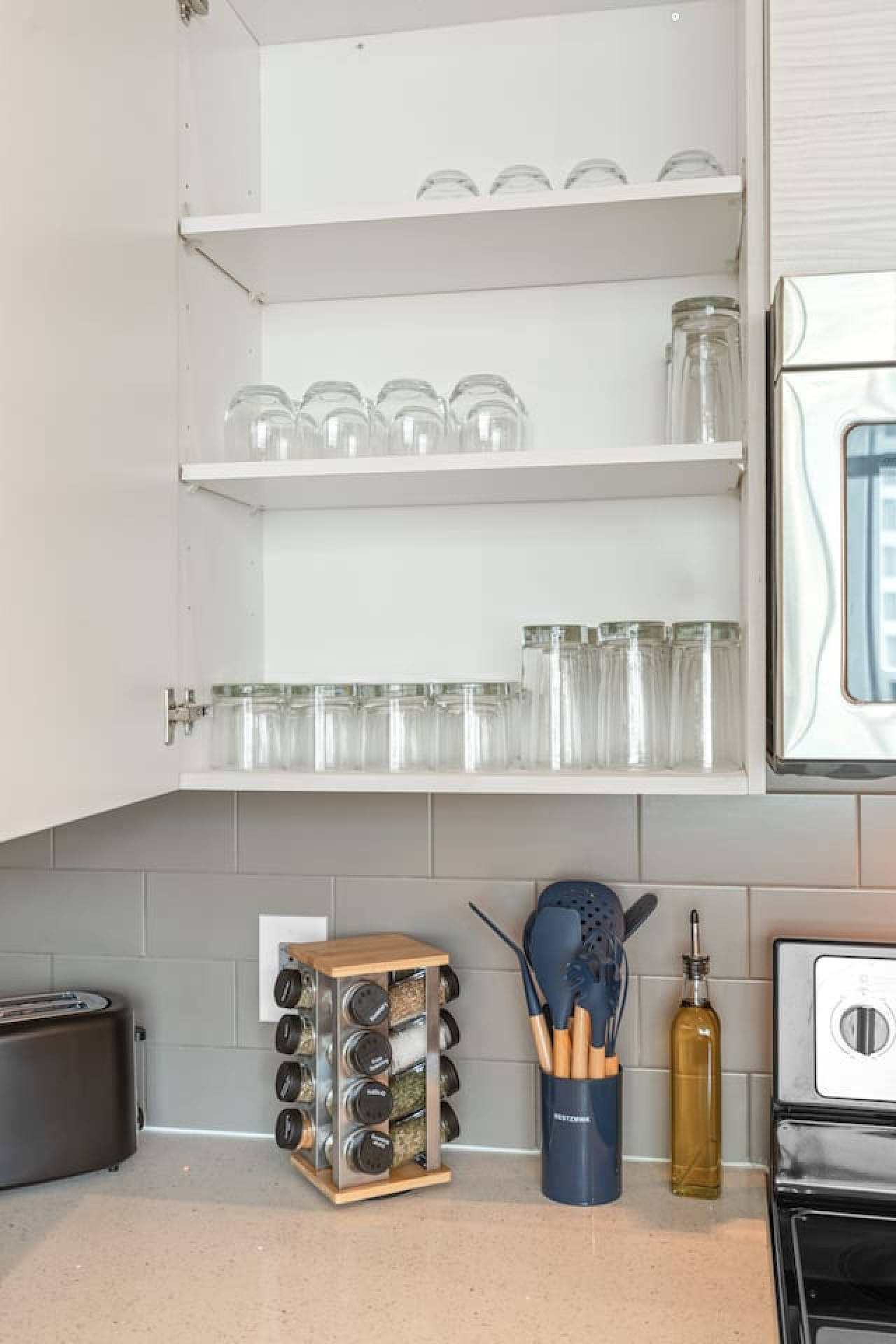 Cabinets stocked with plenty of glassware — wine glasses, tumblers, and drinking glasses for every occasion. Spice rack, utensil set, and olive oil on the counter so you can cook with ease.