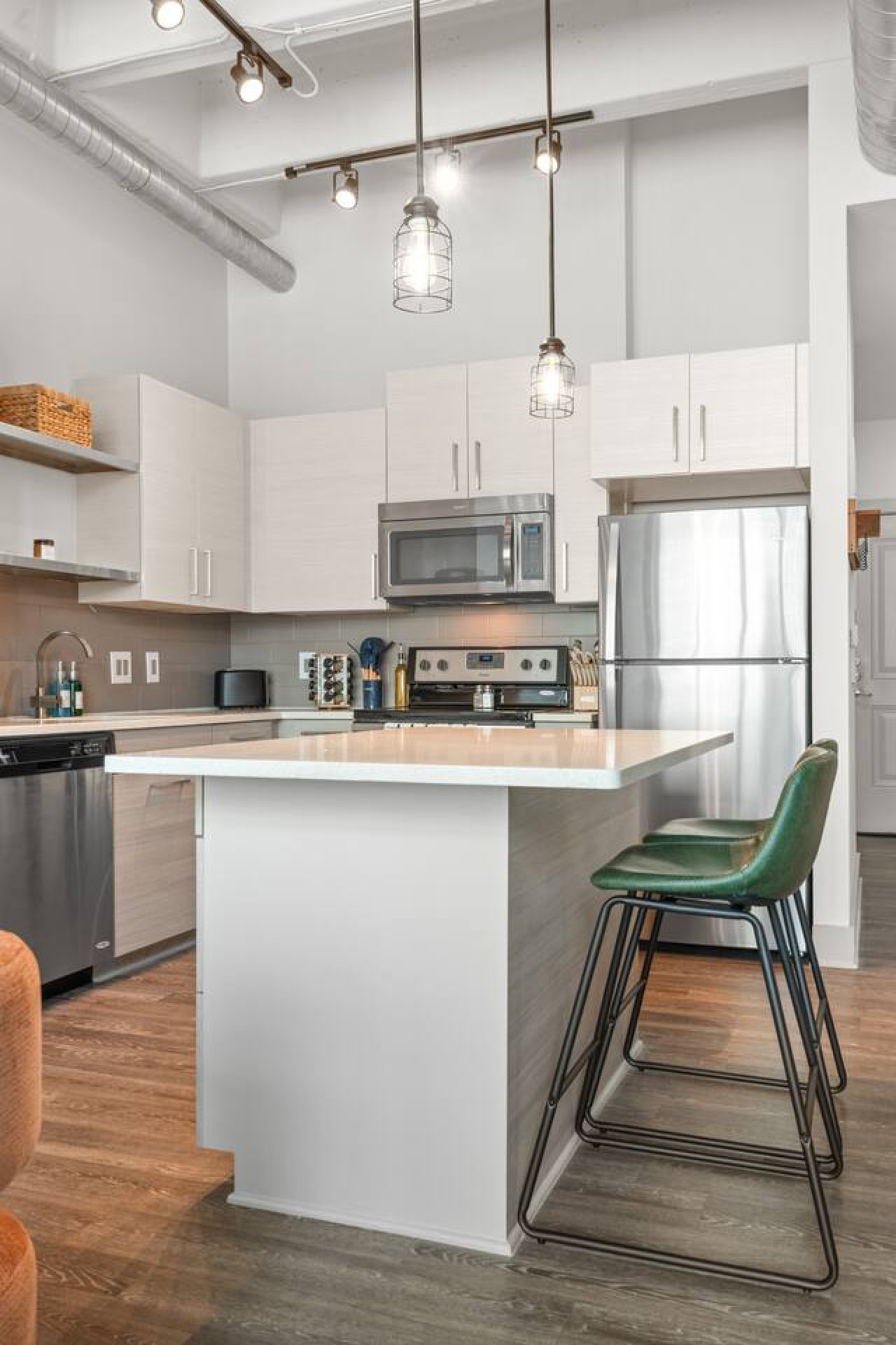 Kitchen island with bar seating under industrial cage pendant lights — perfect for casual meals or morning coffee. Full appliance suite, wine rack, and subway tile backsplash complete this modern loft kitchen.