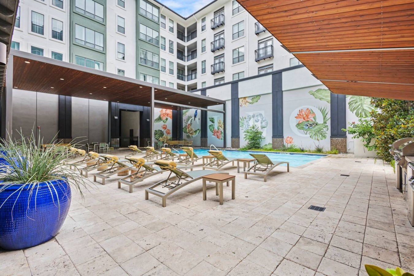 Resort-style pool with lounge chairs, shaded seating, and tropical murals.
