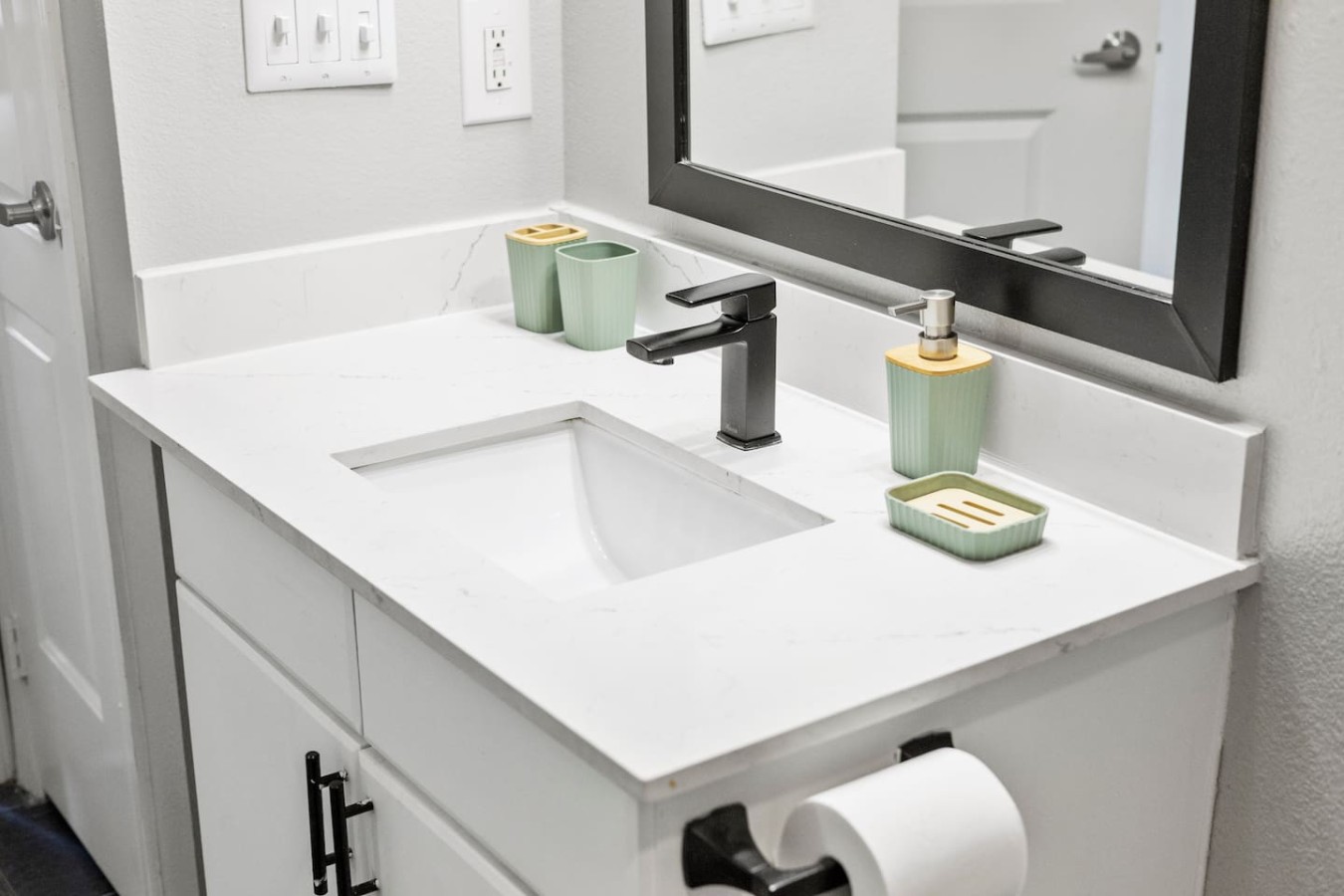 Bathroom vanity with modern faucet and stocked soap and cups.