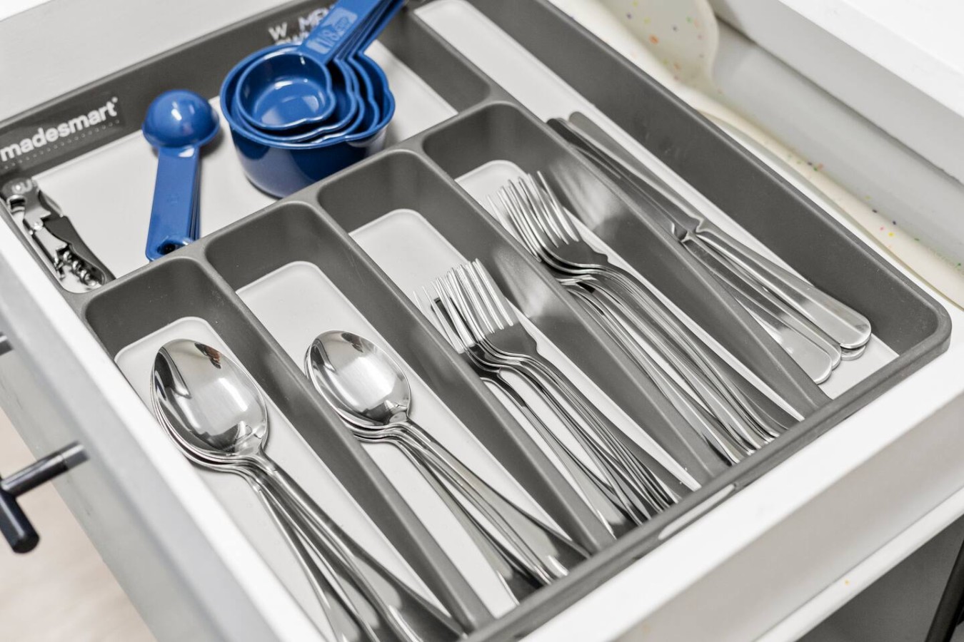 Cutlery drawer with spoons, forks, and measuring tools for cooking.