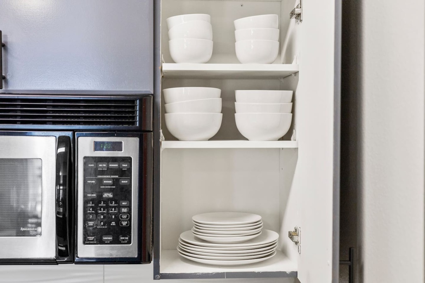 Cabinet stocked with plates, bowls, and microwave.