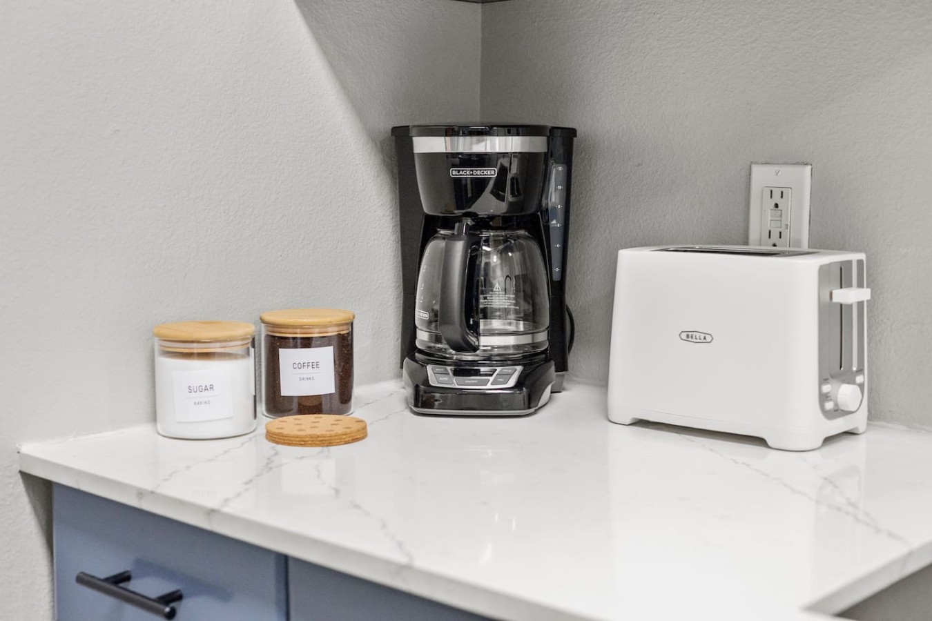 Coffee station with coffee maker, toaster, and jars of sugar and coffee.