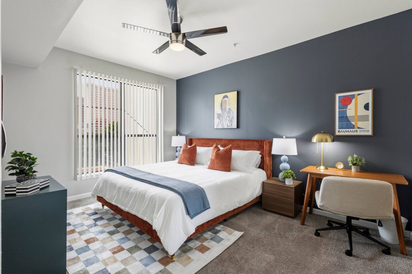 Bright king bedroom with ceiling fan, workspace, and natural light.