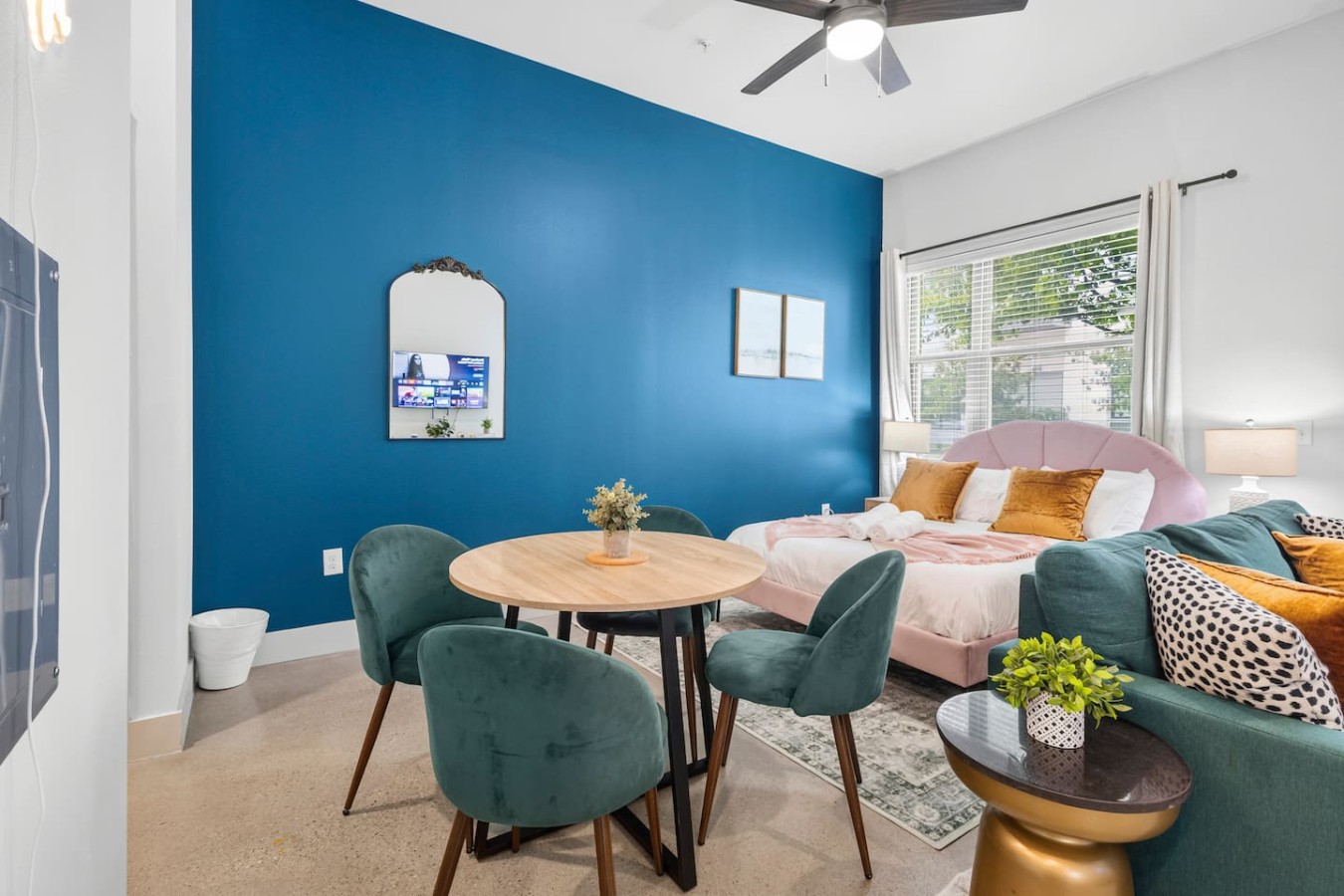 Charming dining corner featuring velvet green chairs and a round wooden table against a striking blue wall.