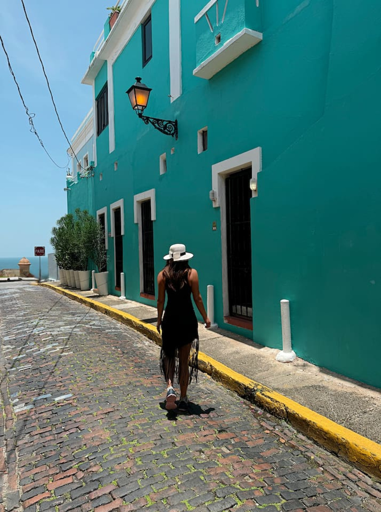 Woman walking down a street in front of a blue building — Ocean Breeze | Old San Juan | Spanish Style, Old San Juan