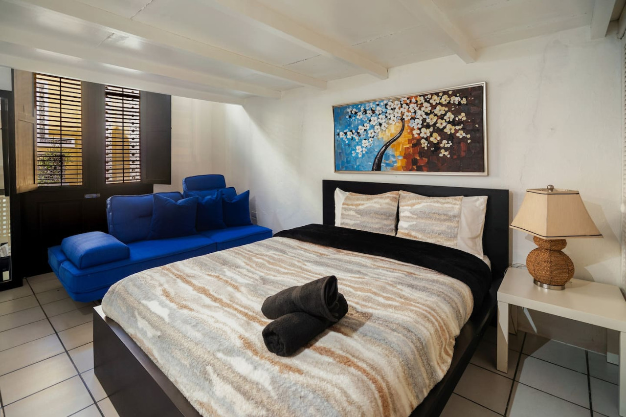 Bedroom with a black bed, blue couch, and a painting on the — Spanish Duplex | Private Patio | Walk to Ocean, Old San Juan
