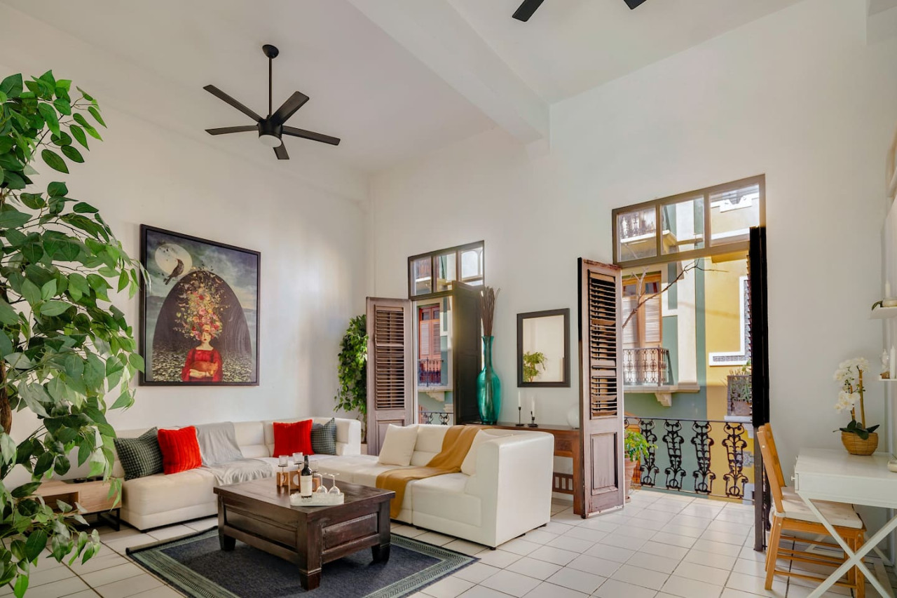 Living room with a couch, coffee table, and a large window — Spanish Duplex | Private Patio | Walk to Ocean, Old San Juan
