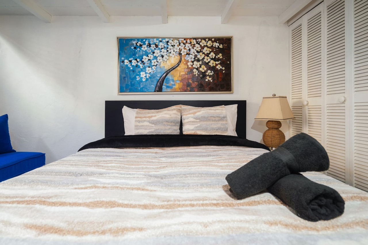 Bedroom with a black bedspread and a painting of a tree on — Spanish Duplex | Private Patio | Walk to Ocean, Old San Juan