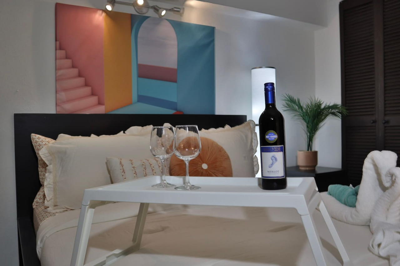 Bedroom with a bed, a table with two wine glasses, and a bottle of wine on it — Puerto Escape | Old San Juan, Old San Juan