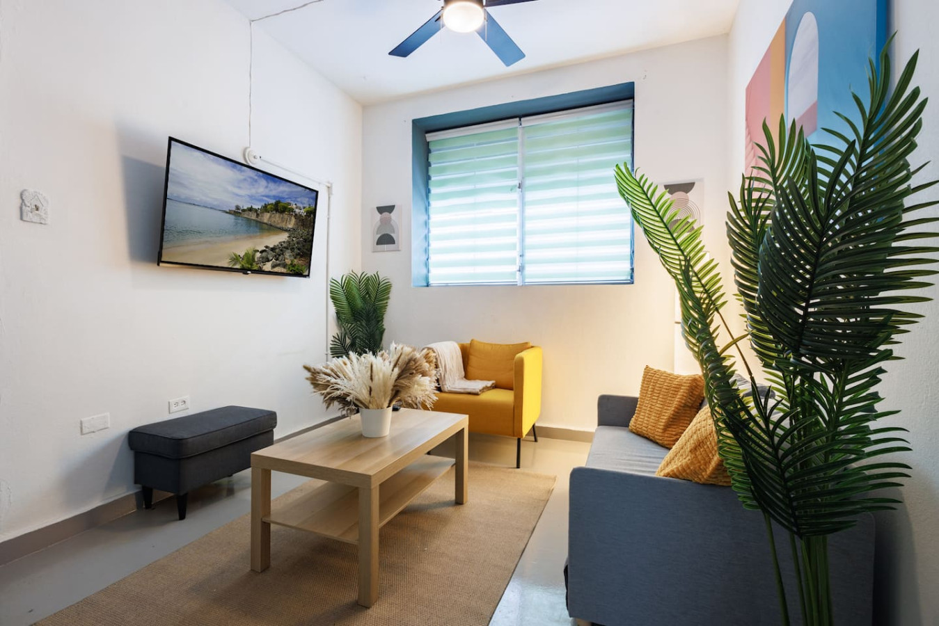Living room with a yellow couch and a table with a vase of flowers on it — Spain Lagoon | San Juan | Private Patio, Santurce