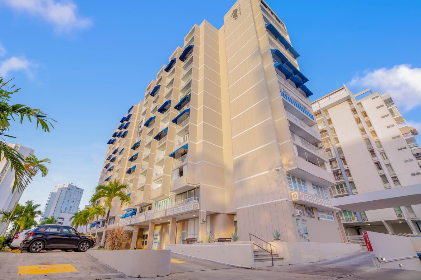 Tall white building with blue balconies and a blue and white striped awning — OceanSide - Pool Balcony, Isla Verde