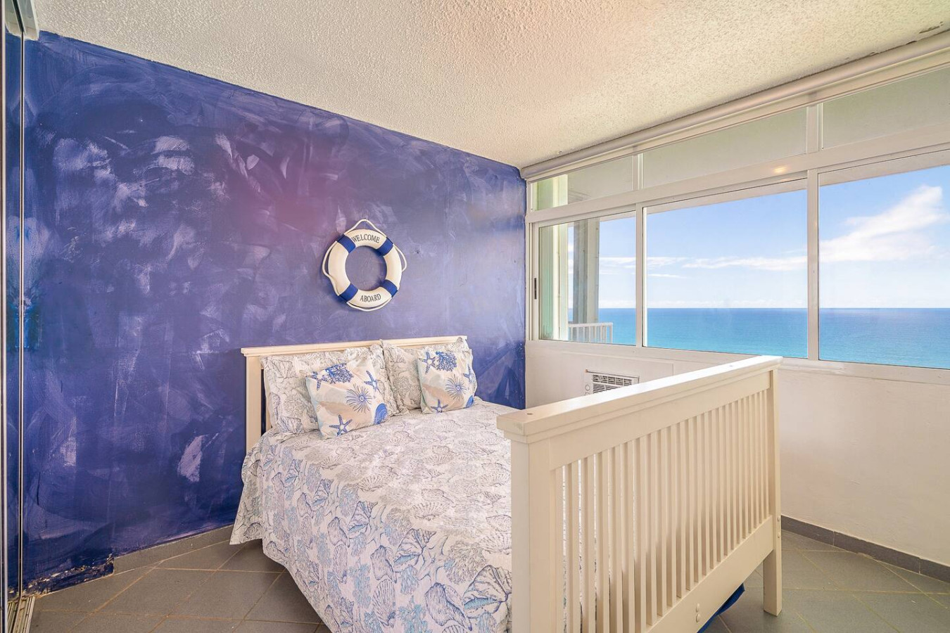 Bedroom with a blue accent wall and ocean-view windows — Captain’s Beachfront Luquillo Beach House