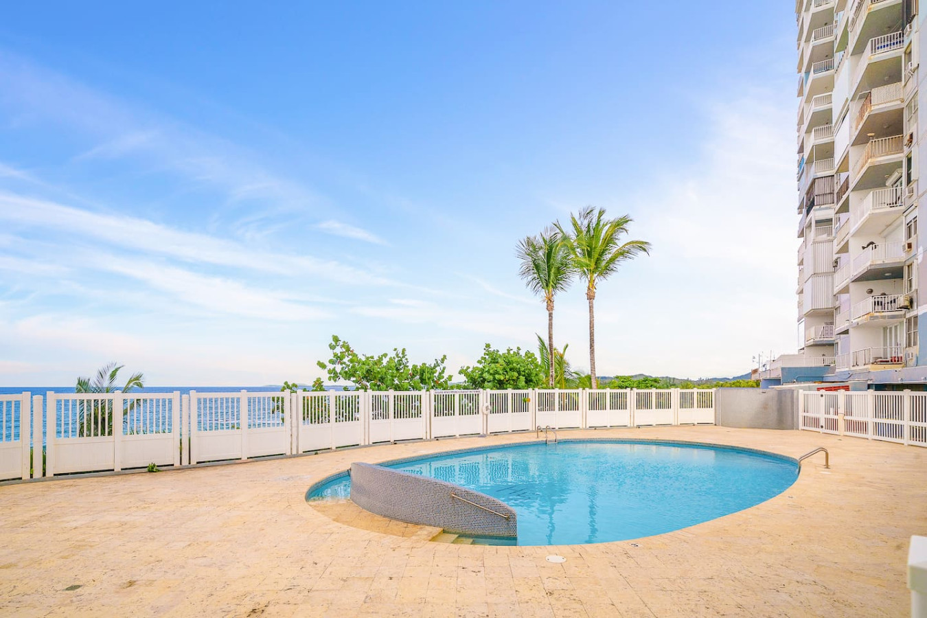 Pool area with a blue swimming pool and a patio with a bench — Captain’s Beachfront Luquillo Beach House, Luquillo
