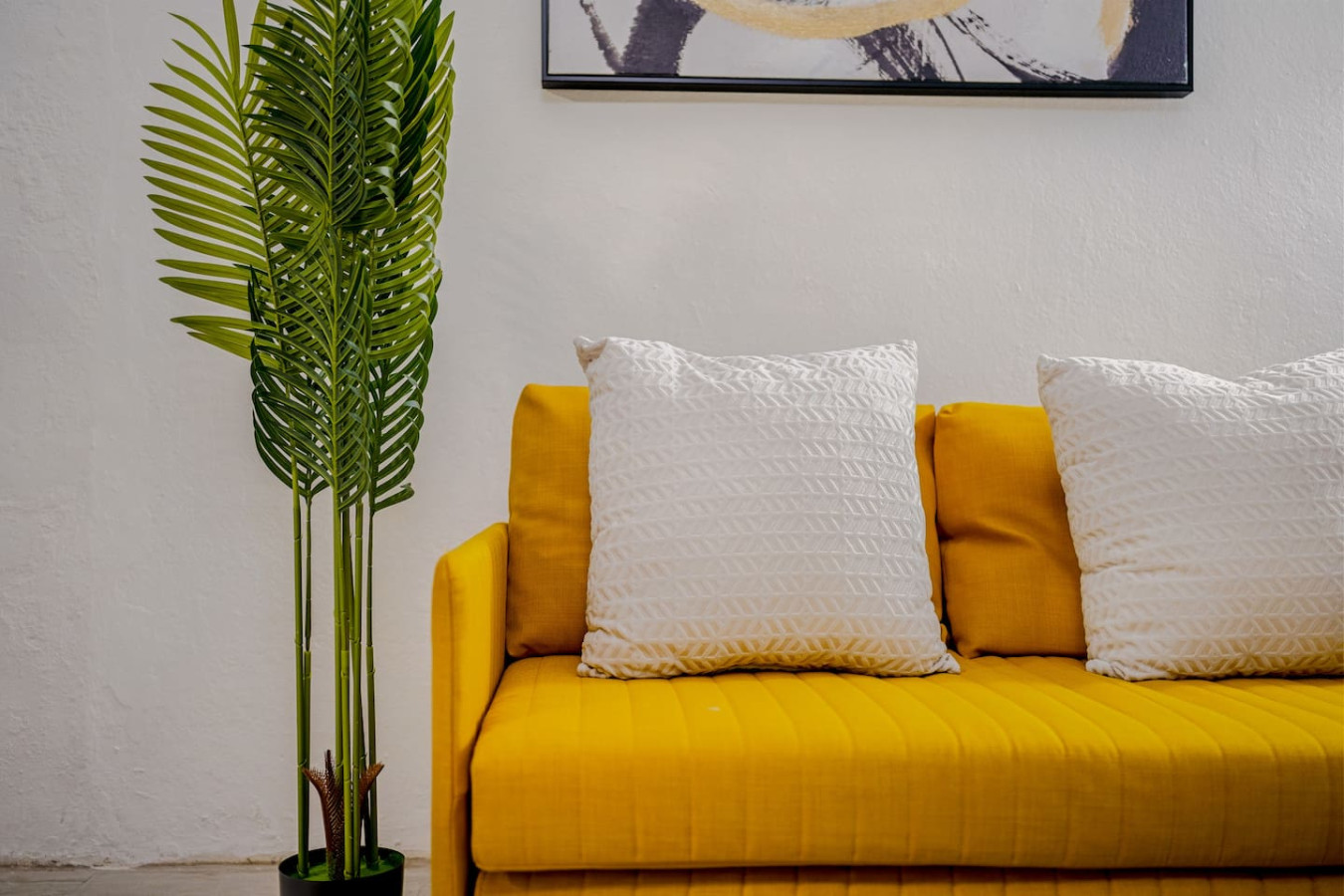 Yellow couch with two white pillows and a potted plant in front of it — Loft La Luz - Old San Juan, Old San Juan