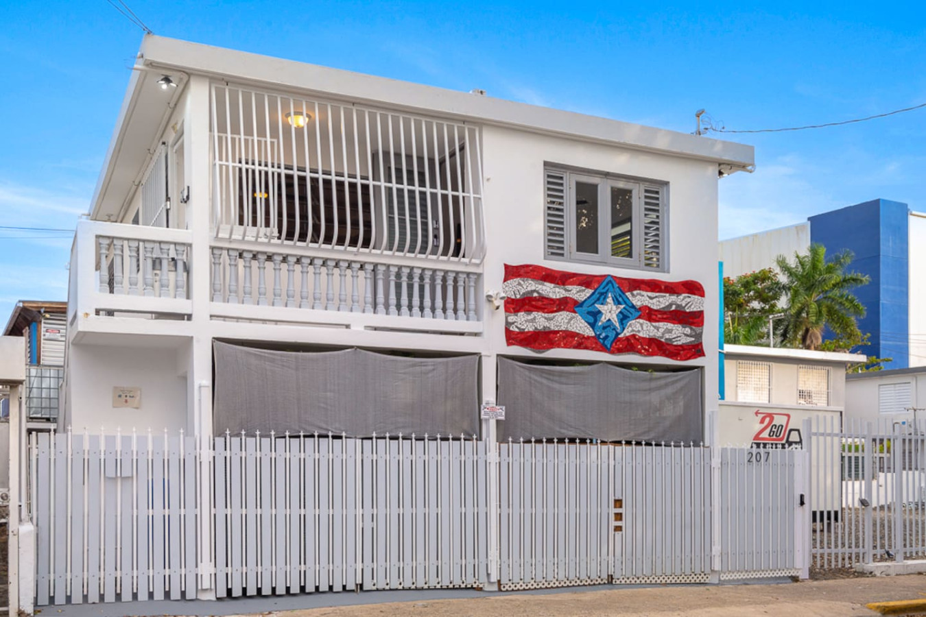 White house with a red, white and blue flag on the front balcony — Casa Juno I: Private Courtyard Studio, Santurce