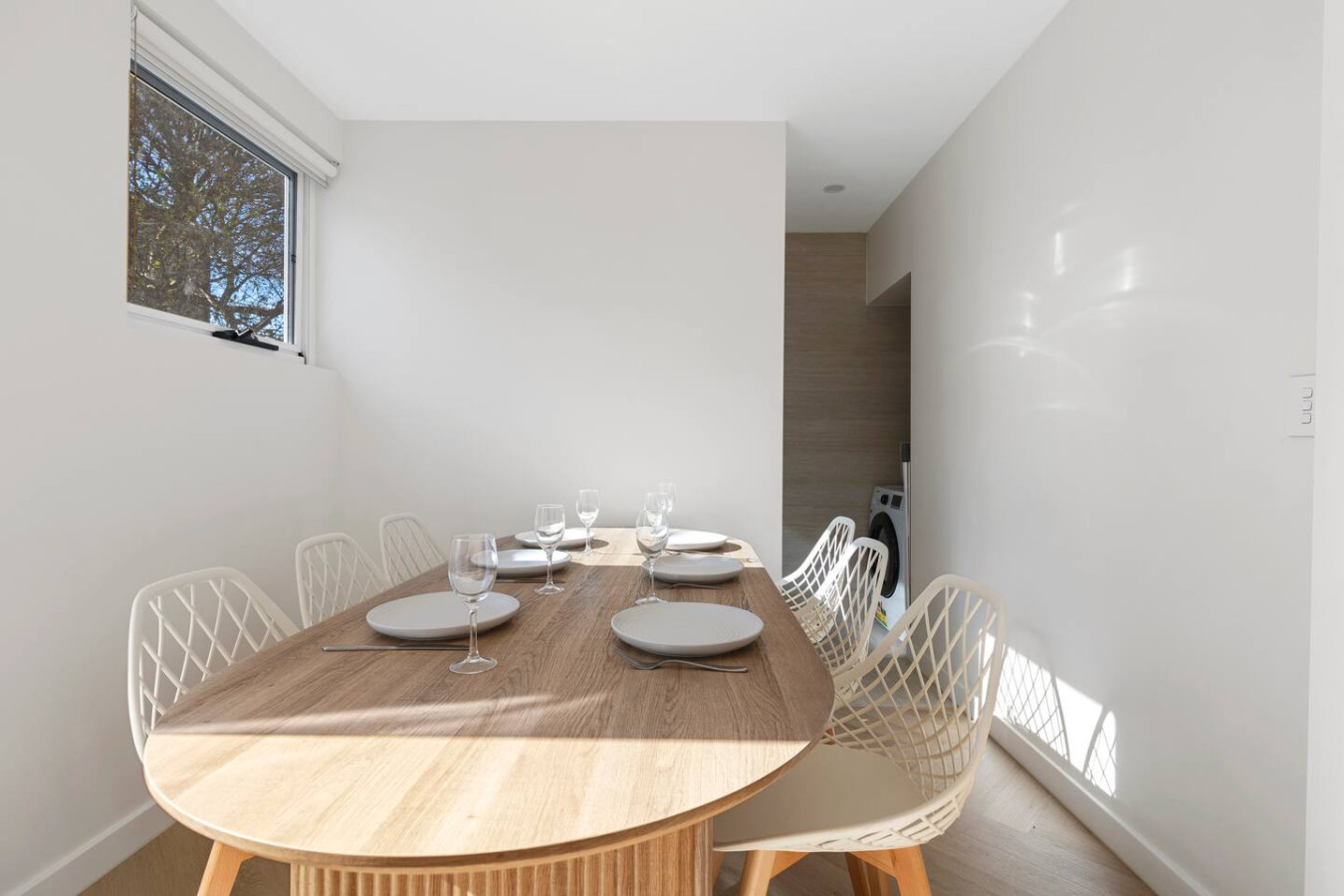 A beautifully set dining table bathed in natural light, with a hidden laundry nook in the background—combining functionality with elegance. By Superhostly