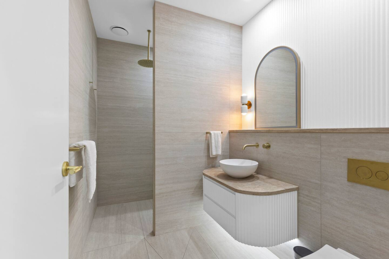Elegant bathroom with a spa-like feel, featuring warm tones, gold accents, and a luxurious rain shower. By Superhostly
