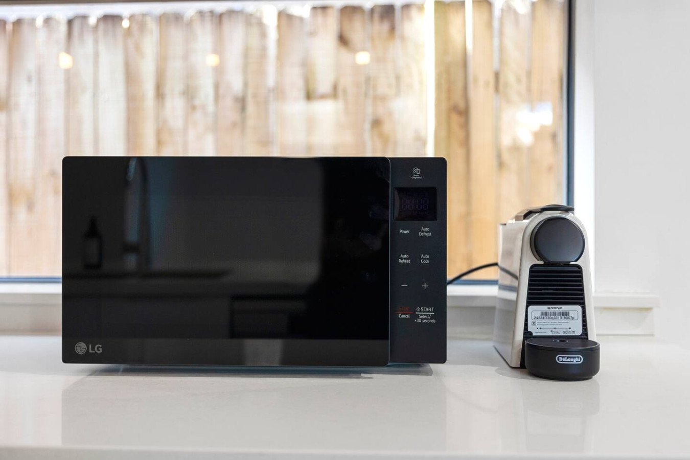 A modern kitchen setup featuring a sleek microwave with a black mirrored finish and a compact Nespresso coffee machine. Positioned on a clean white countertop, the appliances add both style and functionality to the space. By Superhostly